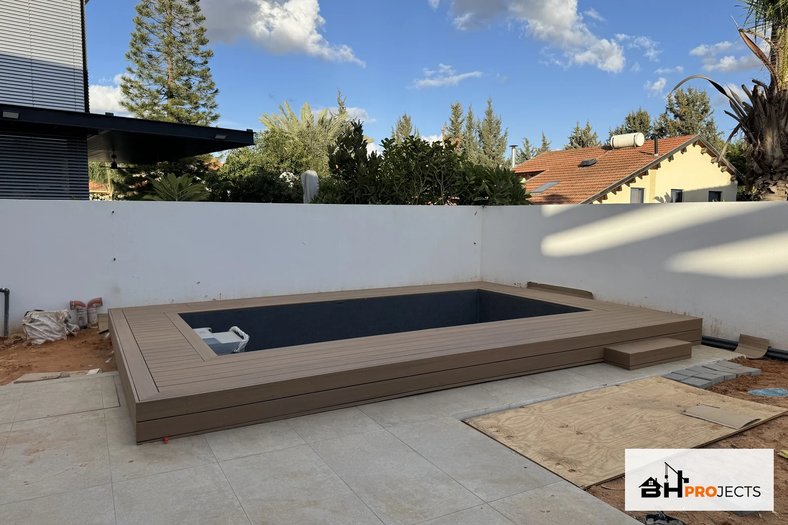 דק TimberTech בגוון Coconut סביב בריכת זרמים ריקה בזמן השלמת סביבת החוץ